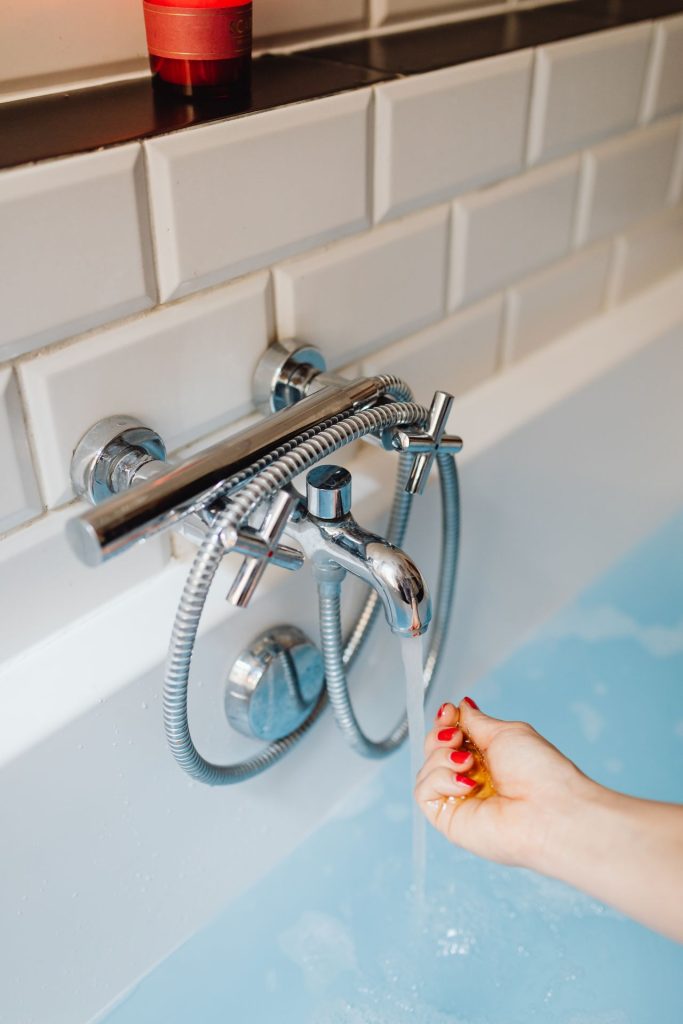 Mano comprobando la temperatura y presión del agua en un grifo de bañera
