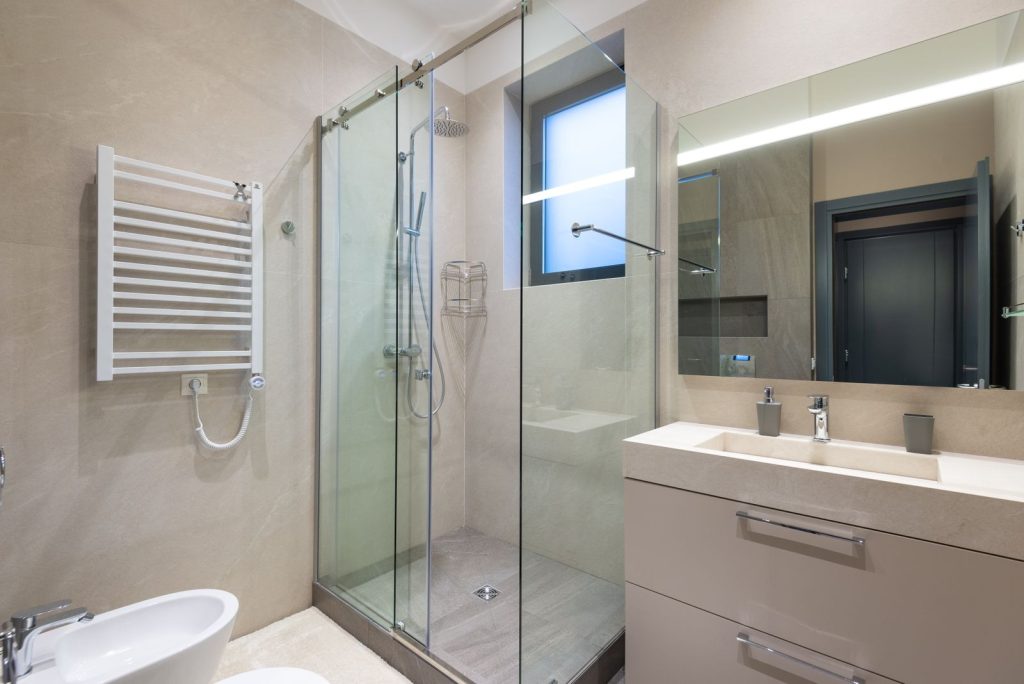 Baño moderno reformado con cabina de ducha de cristal y acabados en tonos neutros